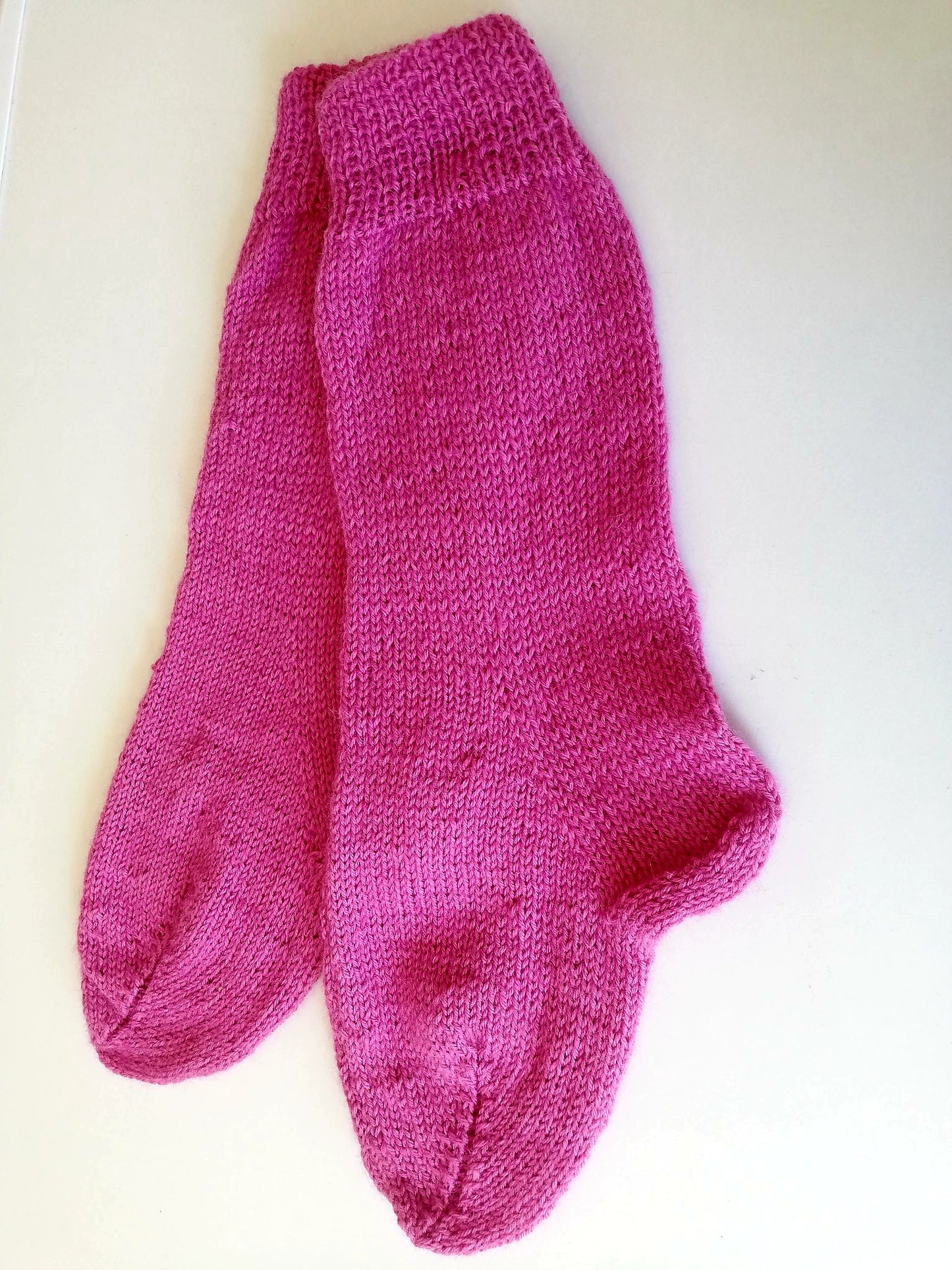 Imahe shows a paid of pink knitted socks laid on a white surface, 