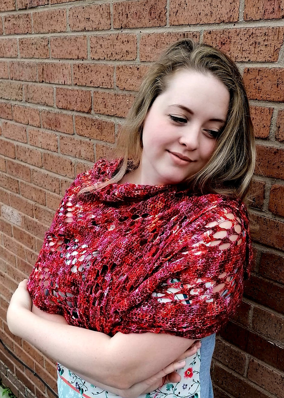 A woman wears a lace panelled crochet shawl across her chest and shoulders. She is looking down with a slight smile. 