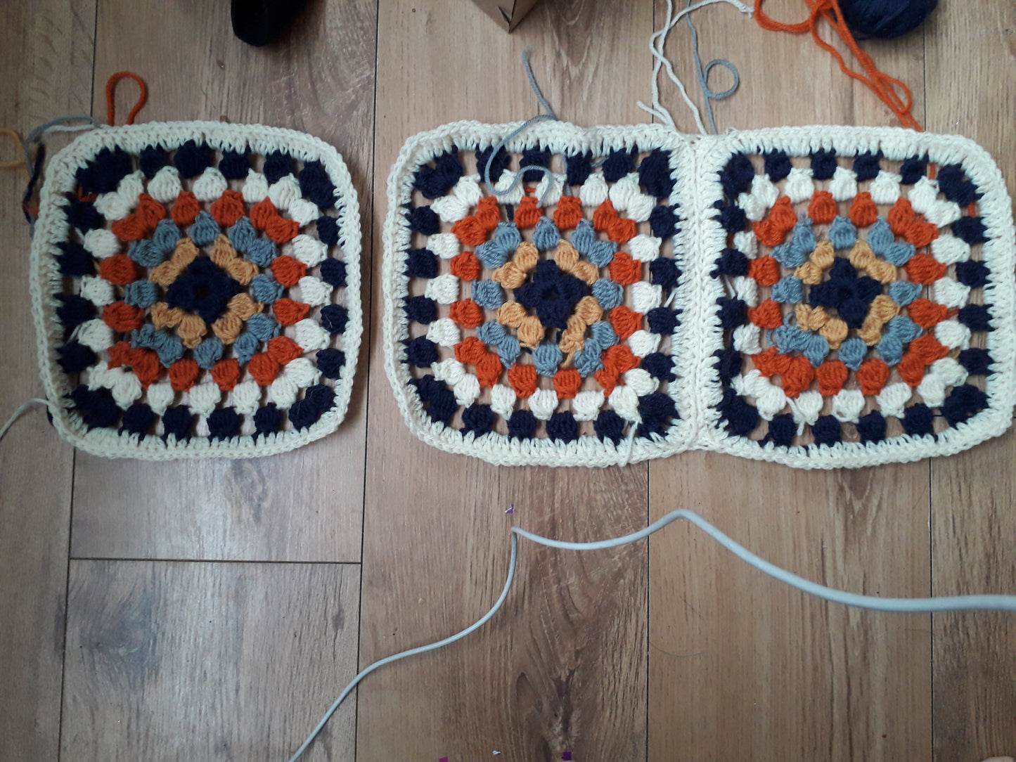 Image shows three crochet granny squares lined up next to each other on a hard wood floor. 