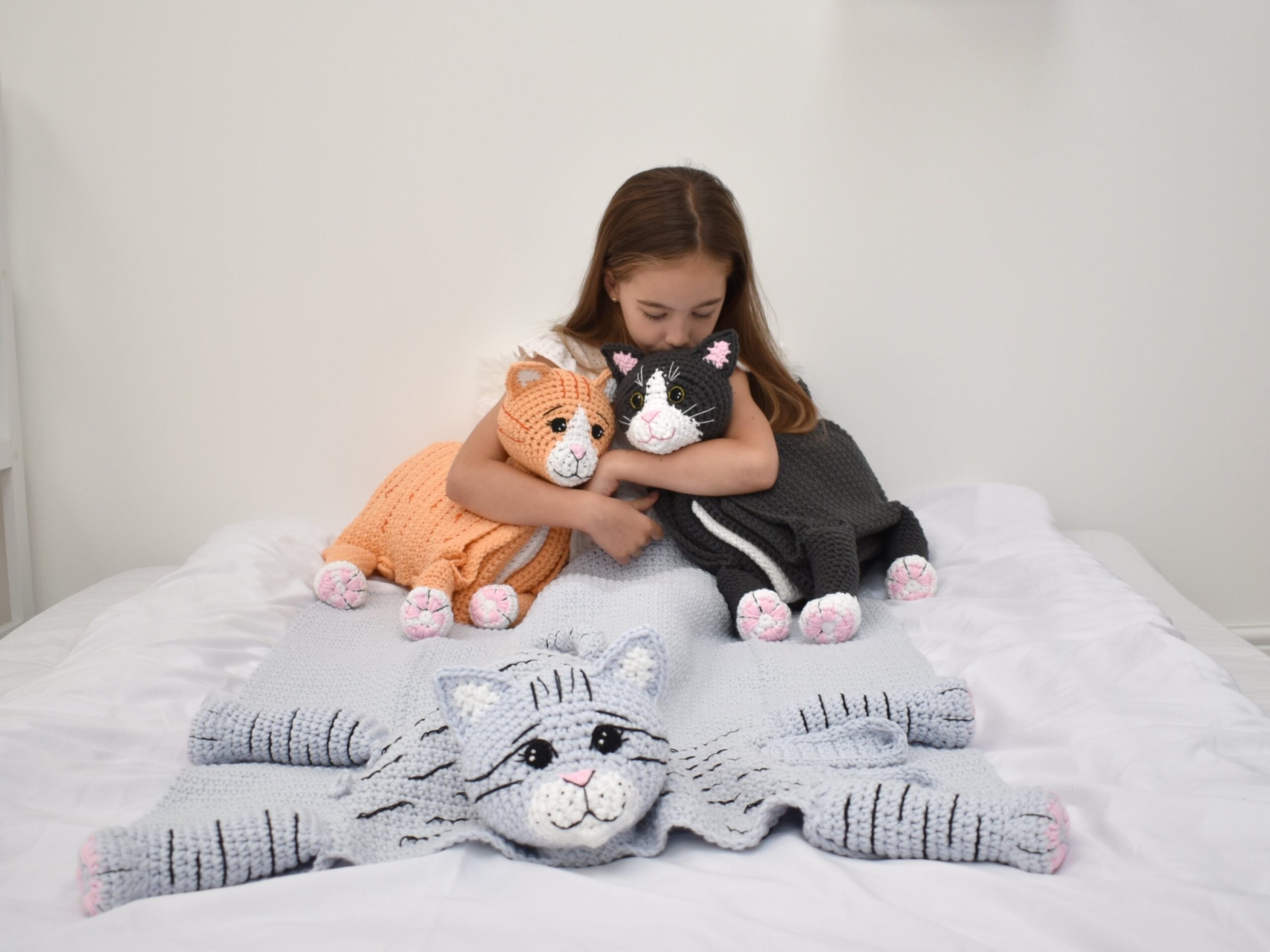 tabby cat crochet blanket kit. Image shows little girl holding two crochet cat toys while using a crochet cat blanket. 