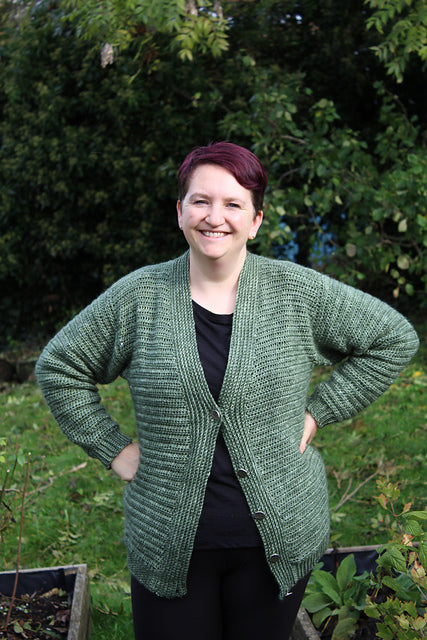 Victoria stood with her hands on her hips, wearing a long green cardigan. Victoria is the owner of Eden Cottage yarns. Here she is pictured wearing her finished Beyond cardigan. 